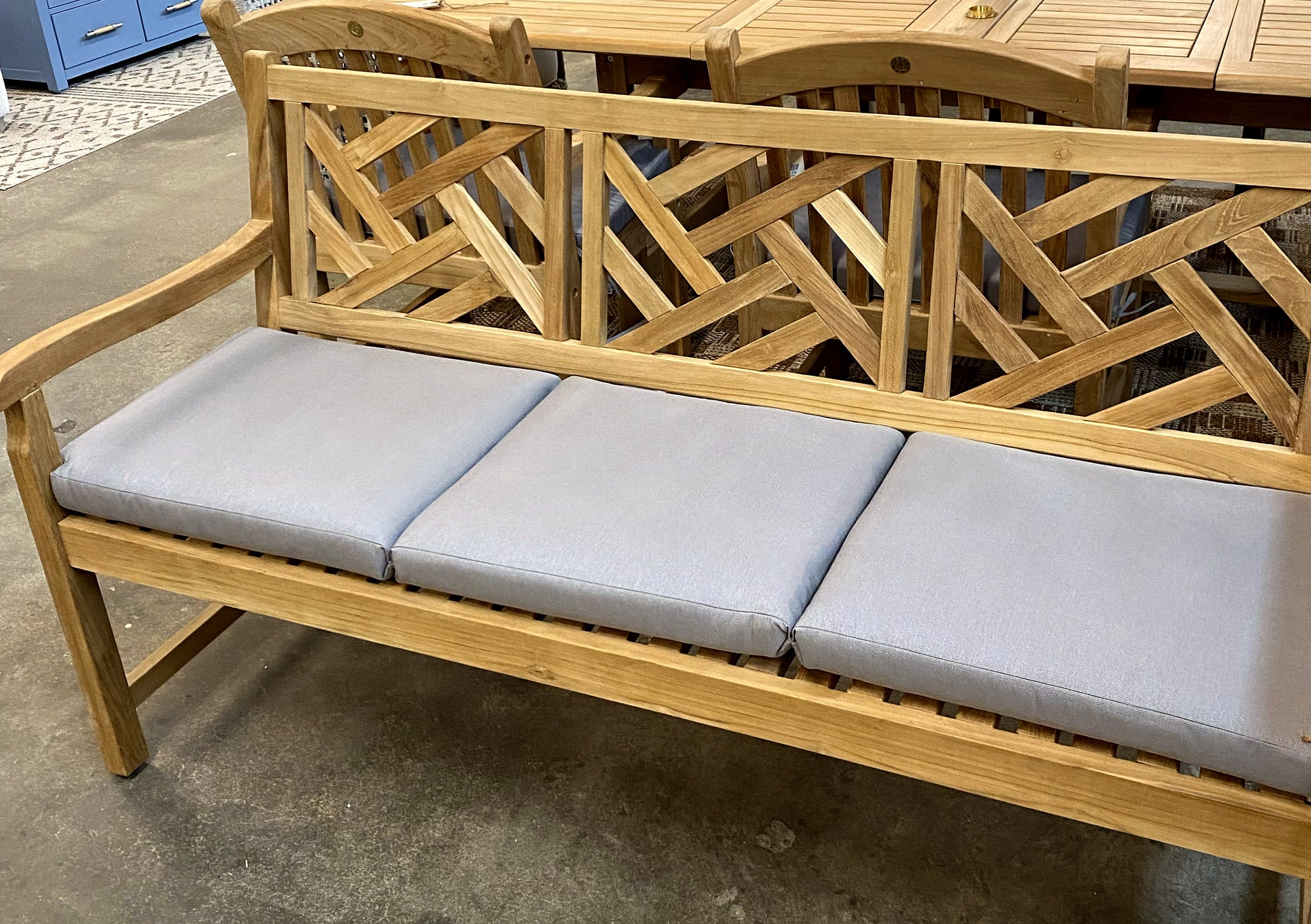 Alor solid teak 60-inch 3-seat outdoor bench in our showroom, shown with its full-length light gray all-weather cushion sectioned into three seats