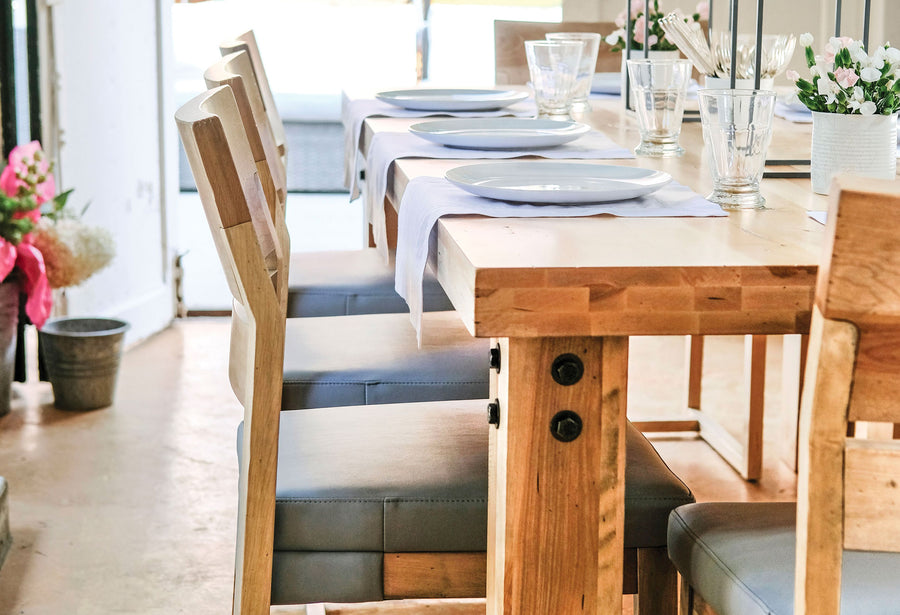 Solid wood trestle dining table with a bench and upholstered chairs in a sunroom
